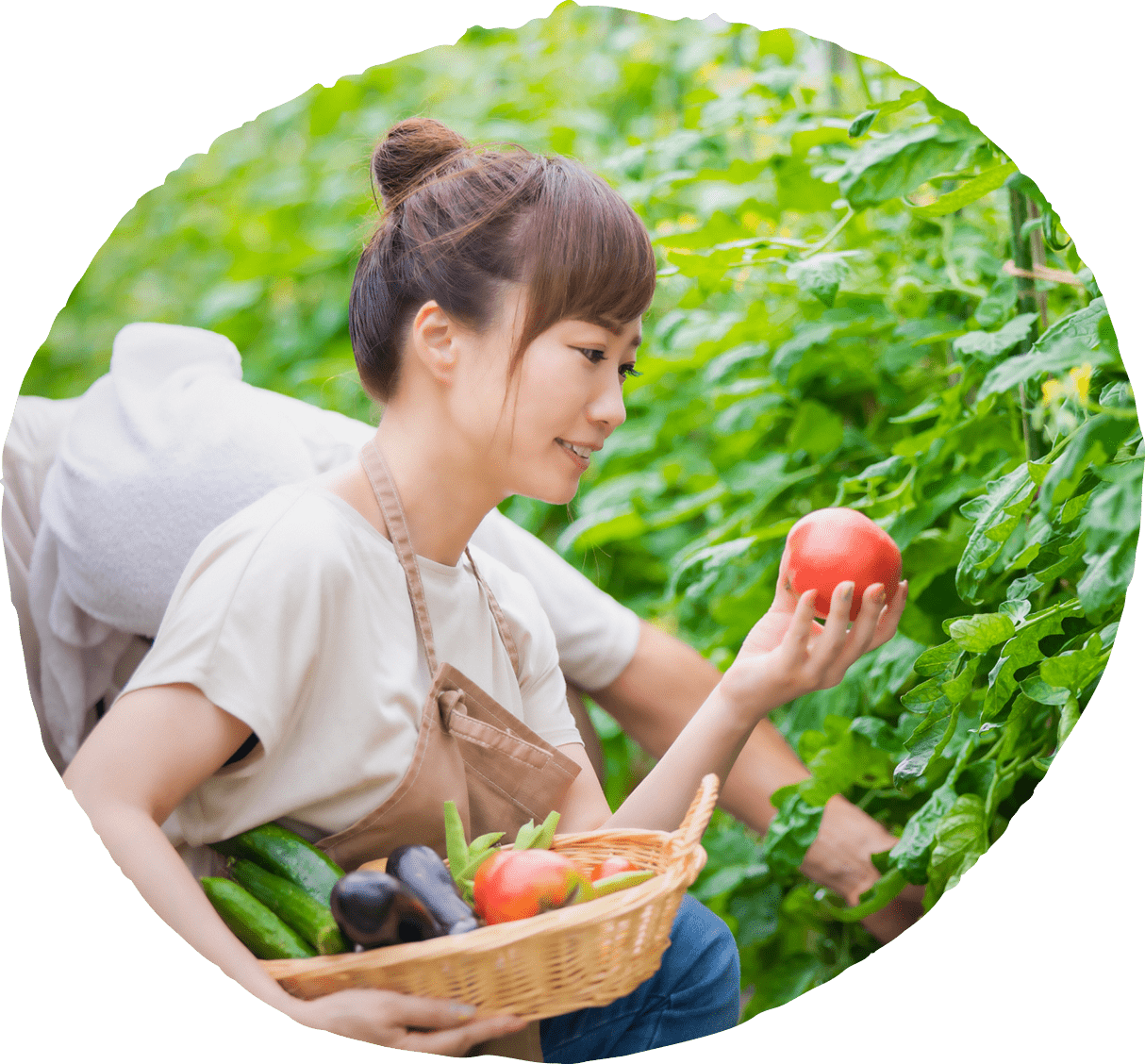 沢山の野菜が入ったかごを片手にトマトを笑顔で見ている女性がいる